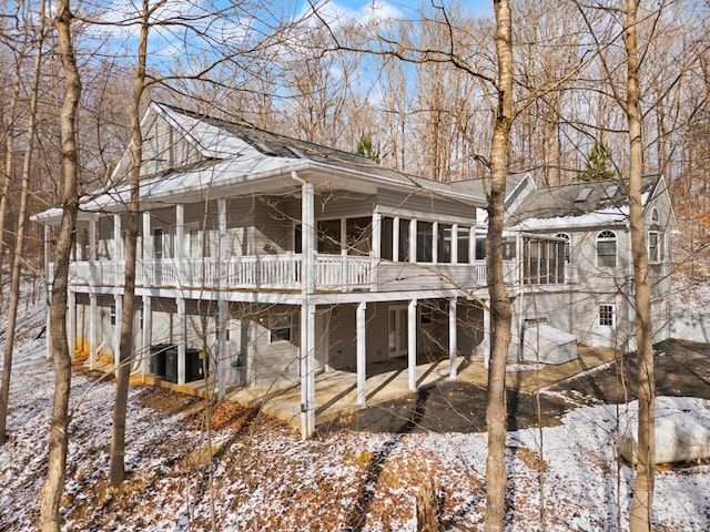 snow covered rear of property featuring central air condition unit, a sunroom, and a patio