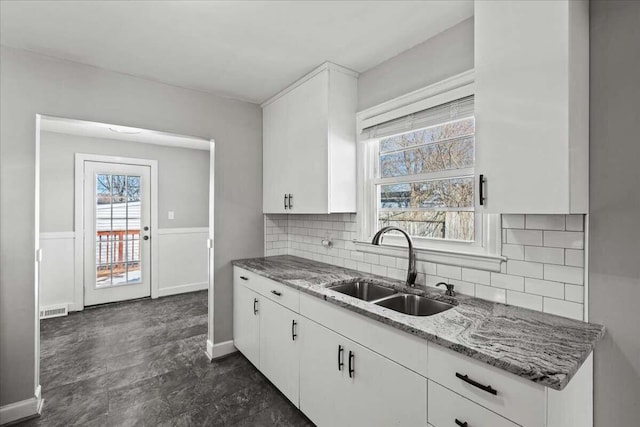 kitchen with white cabinetry, decorative backsplash, sink, and light stone counters