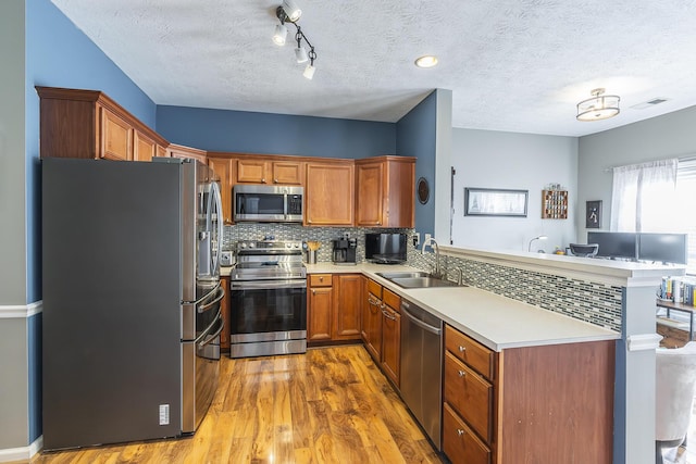 kitchen featuring kitchen peninsula, light hardwood / wood-style flooring, appliances with stainless steel finishes, sink, and tasteful backsplash