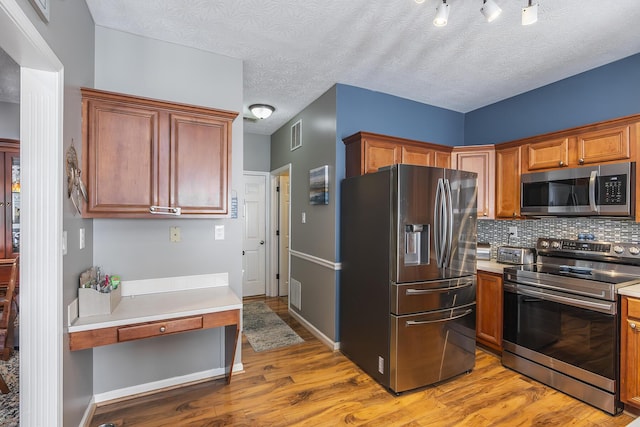 kitchen with light wood-type flooring, backsplash, appliances with stainless steel finishes, and a textured ceiling