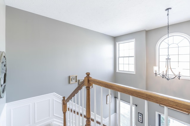 staircase featuring a textured ceiling, a chandelier, and a healthy amount of sunlight