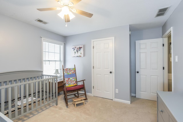 carpeted bedroom featuring ceiling fan and a nursery area