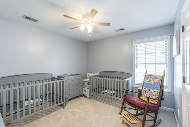 carpeted bedroom with ceiling fan, a nursery area, and multiple windows