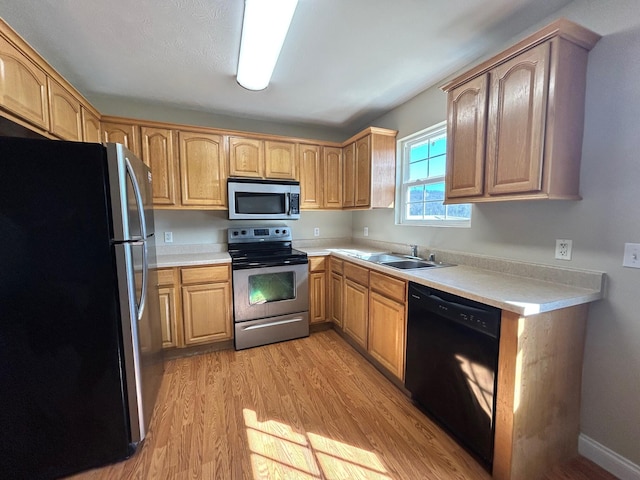 kitchen with appliances with stainless steel finishes, sink, and light hardwood / wood-style flooring