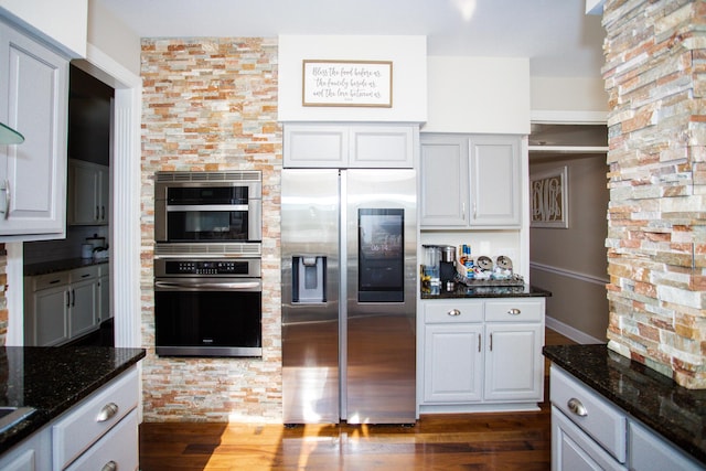 kitchen featuring stainless steel appliances, dark stone counters, and dark wood finished floors