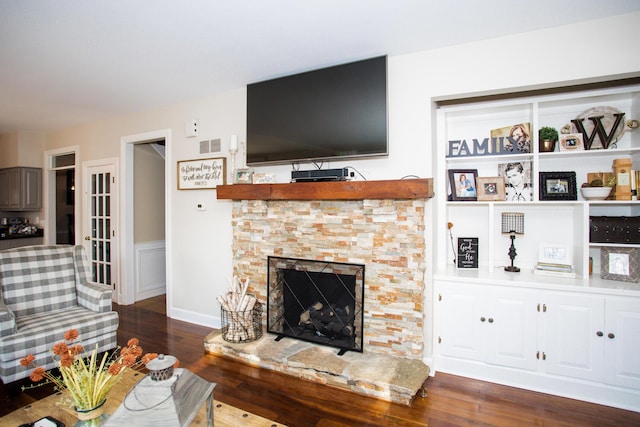 living room featuring visible vents, a fireplace with raised hearth, and wood finished floors