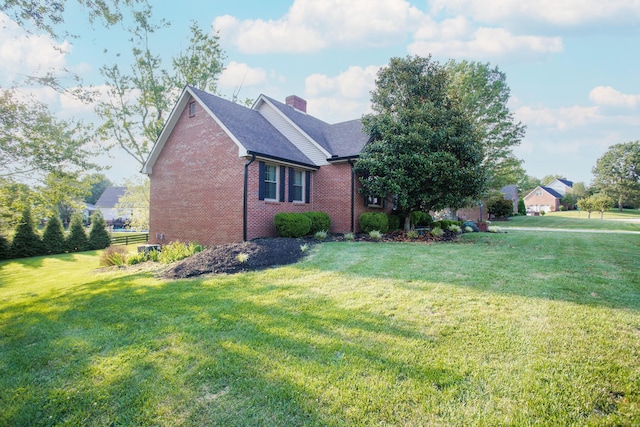 view of home's exterior featuring a yard, a shingled roof, a chimney, and brick siding