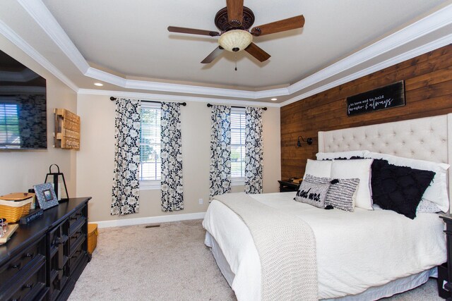 carpeted bedroom with ornamental molding, wood walls, ceiling fan, and a raised ceiling