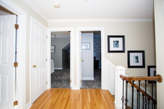 hall with ornamental molding, baseboards, light wood-style flooring, and an upstairs landing