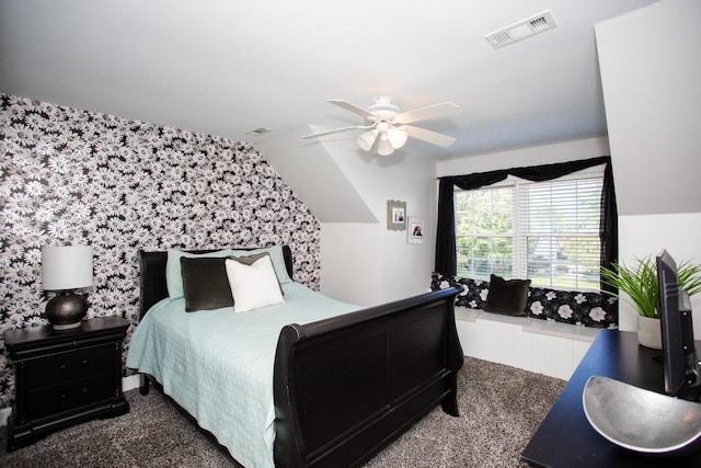 bedroom featuring an accent wall, visible vents, a ceiling fan, vaulted ceiling, and wallpapered walls