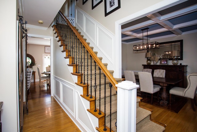 stairs with a decorative wall, ornamental molding, coffered ceiling, beamed ceiling, and hardwood / wood-style floors