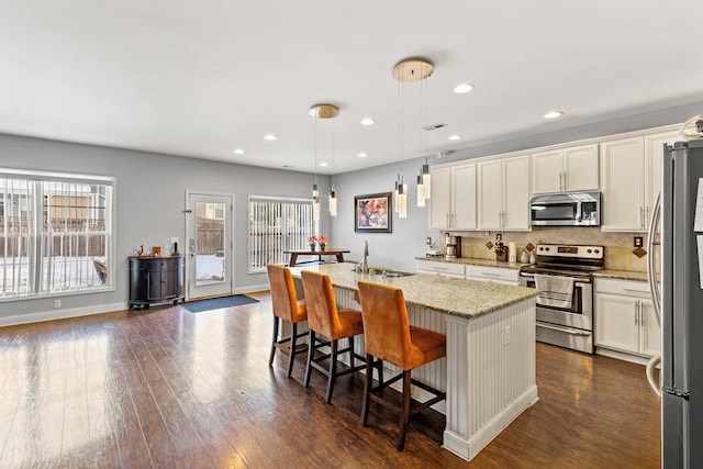 kitchen featuring appliances with stainless steel finishes, pendant lighting, an island with sink, a kitchen bar, and light stone counters