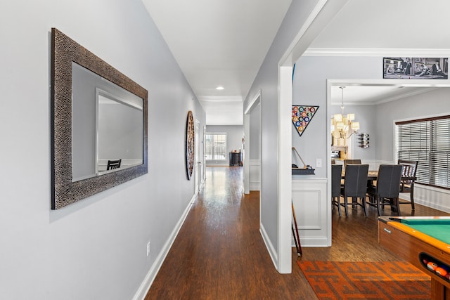 corridor featuring dark wood-type flooring, ornamental molding, and an inviting chandelier