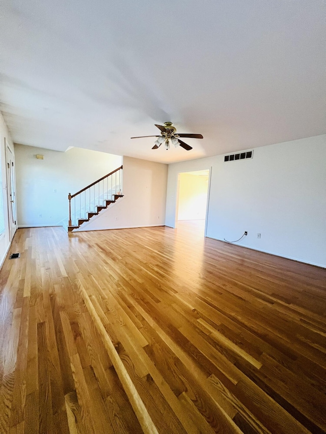 unfurnished living room with wood finished floors, visible vents, and stairs