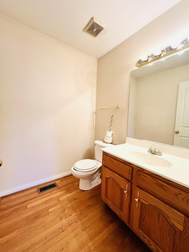 half bathroom with visible vents, vanity, toilet, and wood finished floors