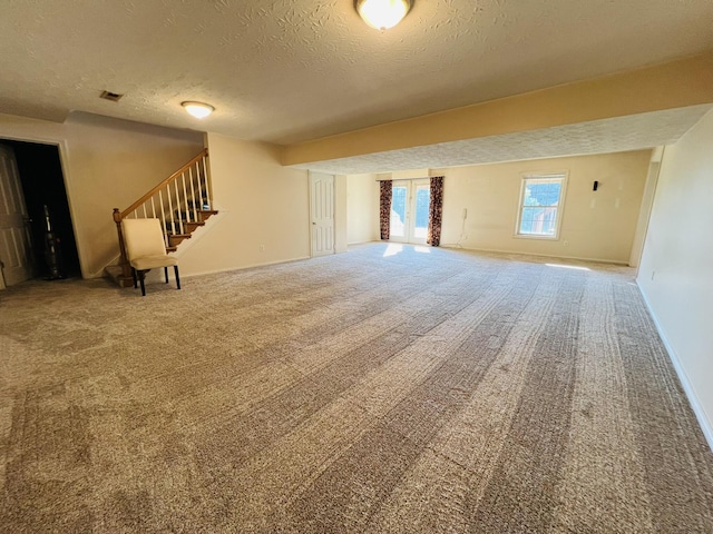 unfurnished living room featuring baseboards, visible vents, stairway, a textured ceiling, and carpet floors