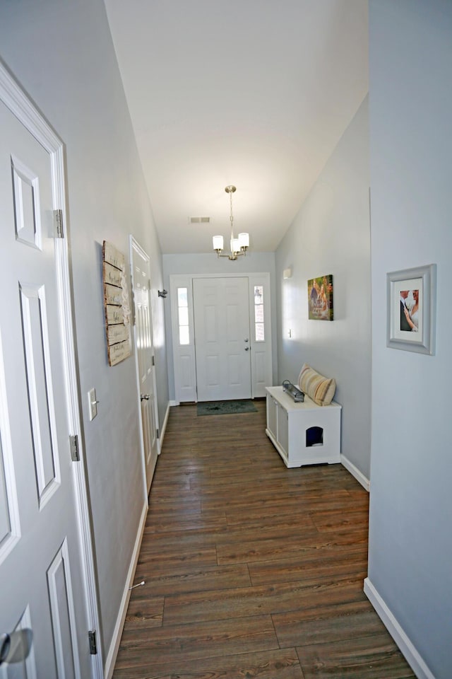 foyer entrance with an inviting chandelier, vaulted ceiling, and dark hardwood / wood-style floors