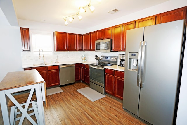 kitchen featuring appliances with stainless steel finishes, sink, light hardwood / wood-style floors, and decorative backsplash