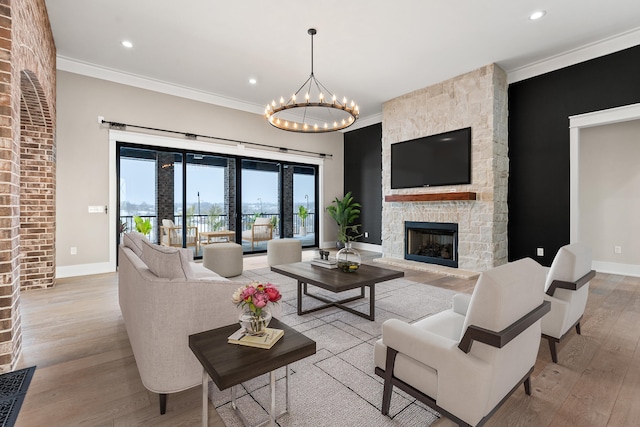 living room featuring light hardwood / wood-style floors, crown molding, a notable chandelier, and a fireplace