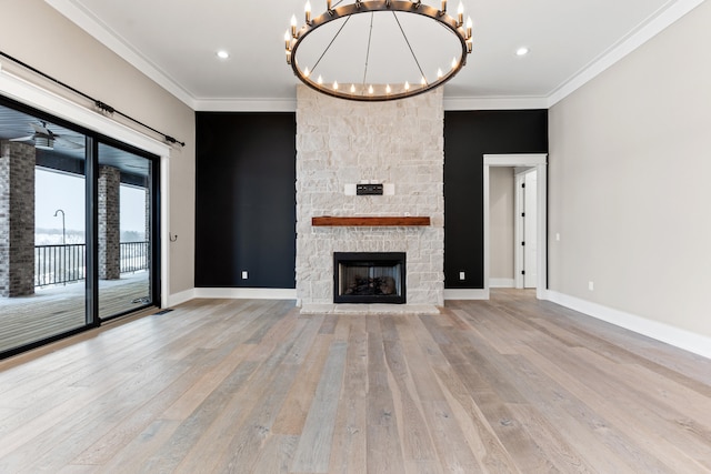 unfurnished living room with light wood-type flooring, a stone fireplace, crown molding, and an inviting chandelier