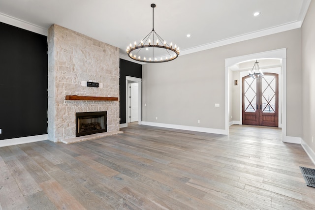 unfurnished living room with hardwood / wood-style floors, french doors, a fireplace, a chandelier, and crown molding