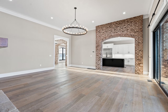 unfurnished living room featuring a notable chandelier, brick wall, crown molding, and light hardwood / wood-style floors