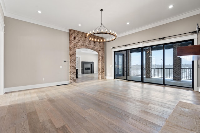 unfurnished living room with crown molding, a brick fireplace, light hardwood / wood-style flooring, and a notable chandelier