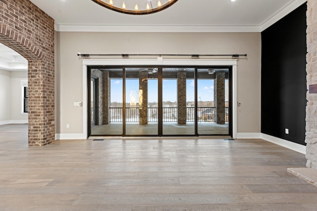 empty room with a notable chandelier, light hardwood / wood-style flooring, and crown molding