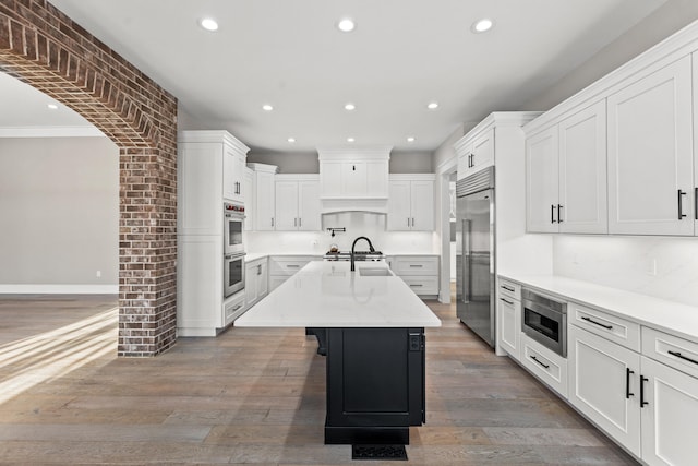 kitchen featuring built in appliances, white cabinetry, a center island with sink, and dark hardwood / wood-style floors