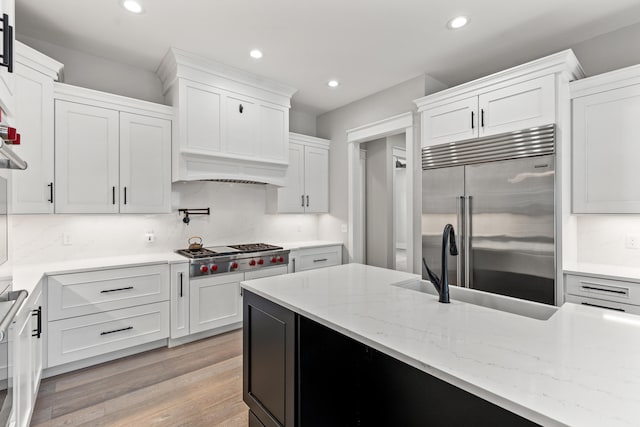 kitchen with premium range hood, light wood-type flooring, white cabinetry, decorative backsplash, and stainless steel appliances