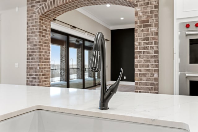 kitchen with light stone countertops, stainless steel double oven, and ornamental molding