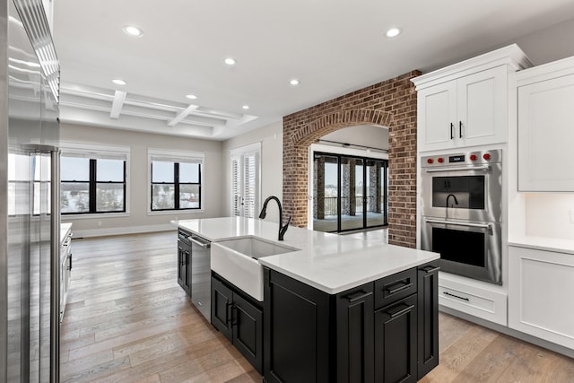 kitchen featuring a center island with sink, white cabinetry, beam ceiling, coffered ceiling, and stainless steel appliances