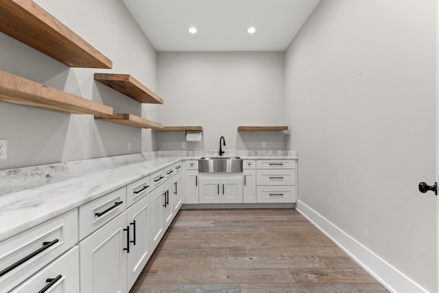 kitchen with light stone counters, sink, white cabinetry, and light hardwood / wood-style floors