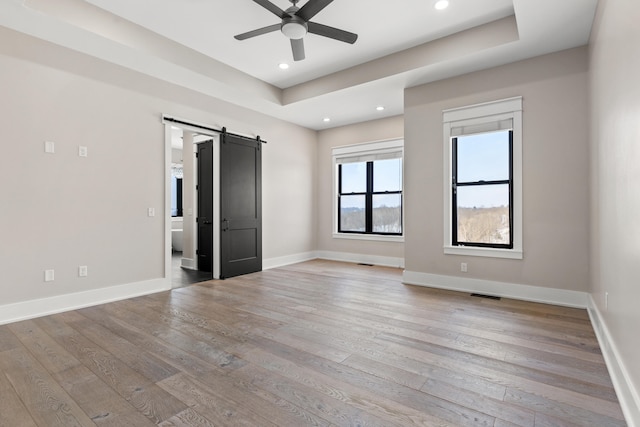 empty room with light hardwood / wood-style floors, a raised ceiling, ceiling fan, and a barn door