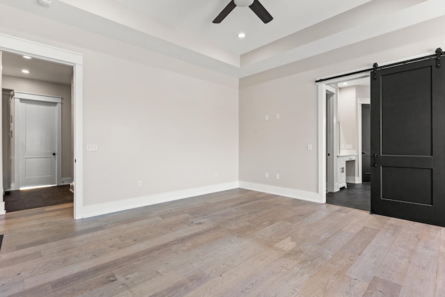 unfurnished bedroom with ceiling fan, light hardwood / wood-style flooring, and a barn door