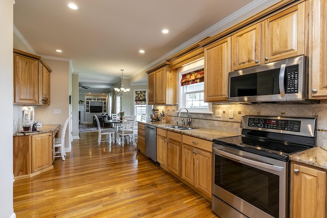 kitchen with decorative light fixtures, sink, light hardwood / wood-style floors, stainless steel appliances, and light stone countertops