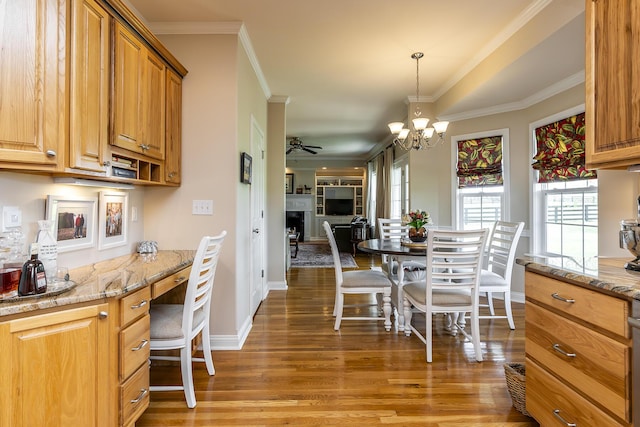 kitchen featuring dark hardwood / wood-style floors, pendant lighting, built in desk, ornamental molding, and light stone counters