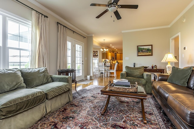 living room with ornamental molding, ceiling fan with notable chandelier, and light hardwood / wood-style floors