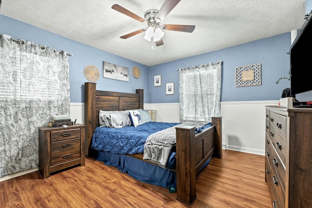 bedroom featuring multiple windows, ceiling fan, hardwood / wood-style flooring, and a textured ceiling