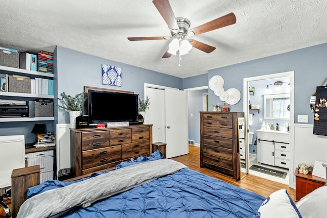 bedroom featuring ensuite bath, ceiling fan, light hardwood / wood-style floors, a textured ceiling, and a closet