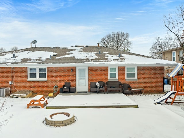 snow covered back of property with central AC, a playground, and a fire pit