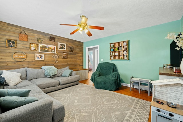 living room featuring ceiling fan, light hardwood / wood-style floors, a textured ceiling, and wood walls