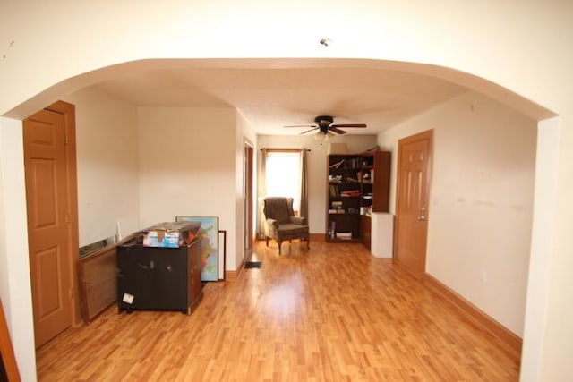 interior space featuring a ceiling fan, arched walkways, and light wood-style flooring