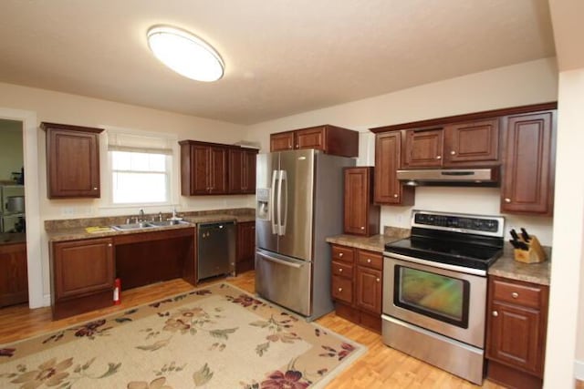 kitchen with light wood-type flooring, under cabinet range hood, appliances with stainless steel finishes, and a sink