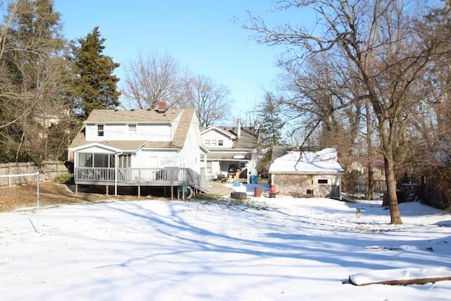 snow covered house featuring a trampoline, a sunroom, fence, and a wooden deck