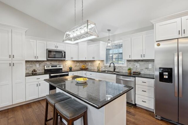 kitchen featuring lofted ceiling, appliances with stainless steel finishes, a sink, and white cabinets