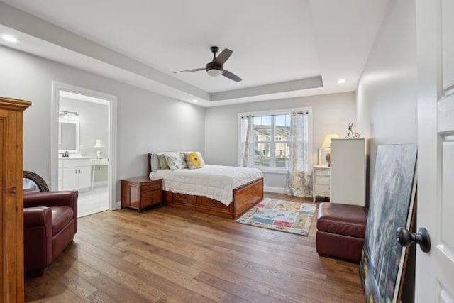 bedroom featuring a ceiling fan, connected bathroom, wood finished floors, a tray ceiling, and recessed lighting