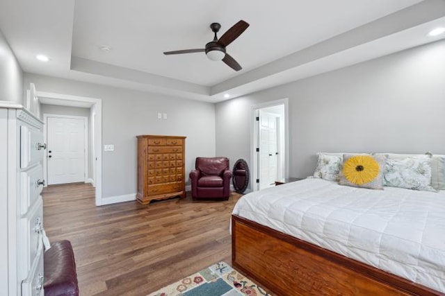 bedroom featuring baseboards, a raised ceiling, a ceiling fan, wood finished floors, and recessed lighting