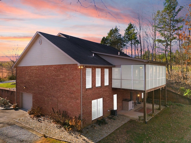 property exterior at dusk with a garage, a sunroom, a patio, and central AC