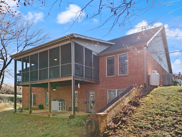 back of property with central AC unit, a sunroom, a lawn, and a patio